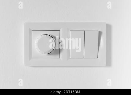 Pair of simple light switches with dimmer. Inexpensive plastic mechanical double switch with thermostat against white wall. Old air conditioner Stock Photo
