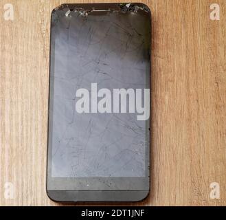 Broken mobile phone lies on a wooden table Stock Photo
