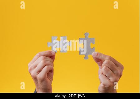 Male hands holding two blank matching puzzle pieces over yellow background. Stock Photo