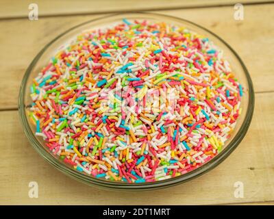 Colored sprinkles for baking decor in a glass plate on a wooden background Stock Photo