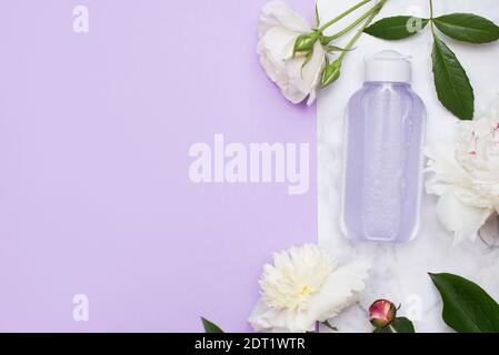 Cosmetic bottle with tonic or micelar water with flowers on marble background and pink copy space. Stock Photo