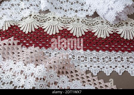 pile of red, white. beige set sail champagne gentle luxury quality guipure, lace fabric on gray background. use for sew clothes linen decoration. Stock Photo