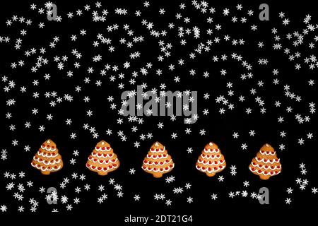 green fir branches as a frame and cookies shaped christmas tree and many white snowflakes on a black chalkboard background. abstract mockup with copy Stock Photo
