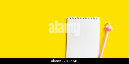 Workspace. Spiral notepad, pink pen on a yellow background. Top view with copy space, flat lay. Stock Photo