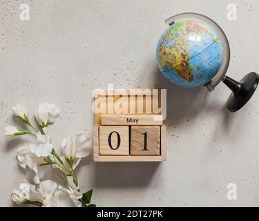 May 1 on a wooden calendar, next to a white flower and a globe. International Day of Workers' Solidarity. Space text. Stock Photo