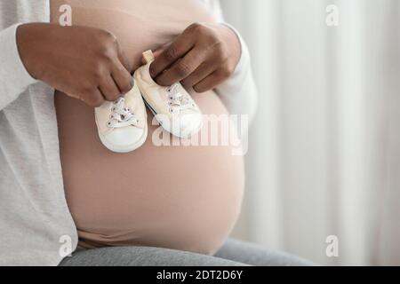 Asian pregnant woman in black undershirt sitting on white bed and touching  her belly in the bedroom with copy space. Pregnancy 7-8 months, motherhood,  love, expectation, care and waiting for her child