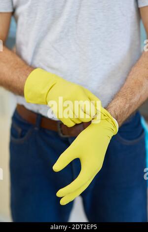 Get started. Close up shot of hands of man, professional male cleaner wearing gloves while getting ready for doing housework Stock Photo