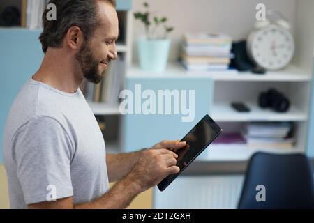 Professional repairman looking cheerful while using digital tablet, standing indoors Stock Photo