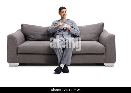 Young man in pajamas seated on a sofa with a cup of espresso coffee isolated on white background Stock Photo