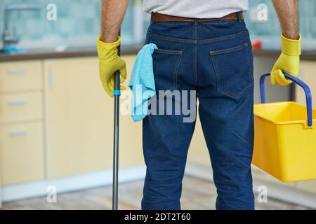 Cleaning guru. Cropped shot of professional male cleaner wearing gloves, holding plastic bucket and mop while getting ready for cleaning floor in the Stock Photo
