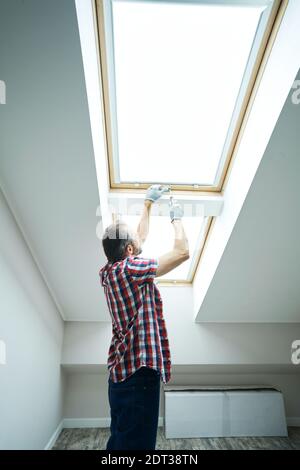 Make your house better. Handyman using screwdriver while fixing or installing a window in a new dry wall attic Stock Photo