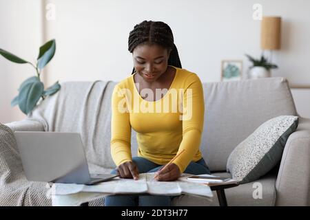 Planning Trip. Happy black woman choosing travel destination on map at home Stock Photo