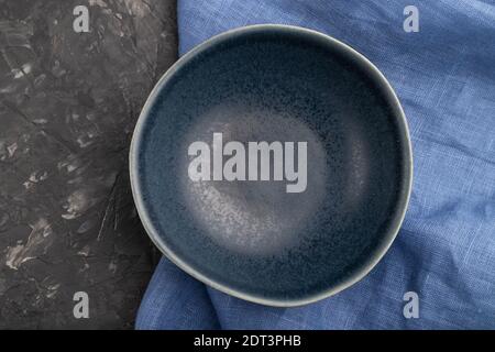 Empty blue ceramic bowl on black concrete background and blue linen textile. Top view, close up, flat lay. Stock Photo