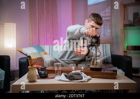 A young man is introduced to the Chinese culture of tea drinking. Brews fragrant raw tea at home. Pour boiling water over tea leaves Stock Photo