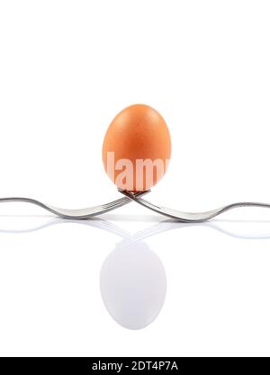 Still life photography. Two forks together create a case for a white egg that balances on them. Egg balanced on forks with white background. Stock Photo