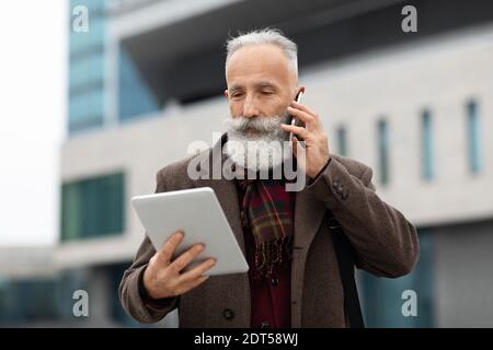 Serious senior man looking at digital tablet, talking on phone Stock Photo