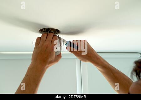 Man hands installing socket for light bulb. Repairs ceiling light indoor home in white room Stock Photo