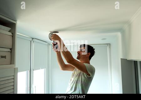 House master male electrician repairs ceiling light indoor home in white room Stock Photo