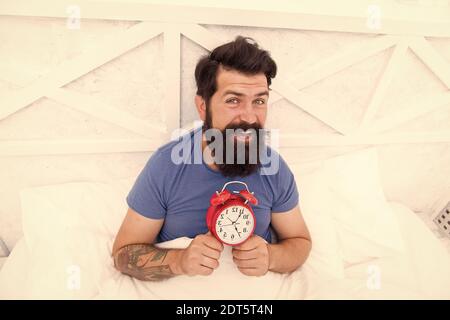 Beginning of awesome day. Wake up early every morning. Health benefits of rising early. Waking up early gives more time. Hipster bearded man in bed with alarm clock. Time to wake up. Healthy habits. Stock Photo