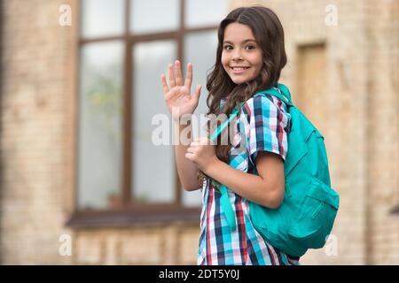 Cute happy girl with long hair in casual style carry travel bag waving goodbye hand gesture outdoors, wanderlust, copy space. Stock Photo