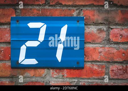 Blue metallic sign on red brick wall with digit 21, Poland. Stock Photo