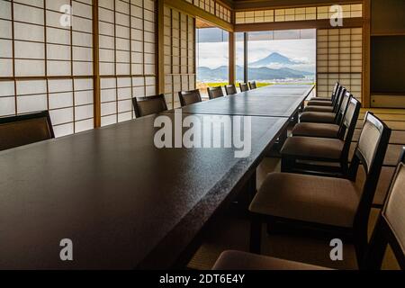 A long table with upholstered chairs is set in a tatami banquet room, with a view of Mount Fuji through sliding shoji doors, Nippondaira Hotel near Shizuoka, Japan. Stock Photo