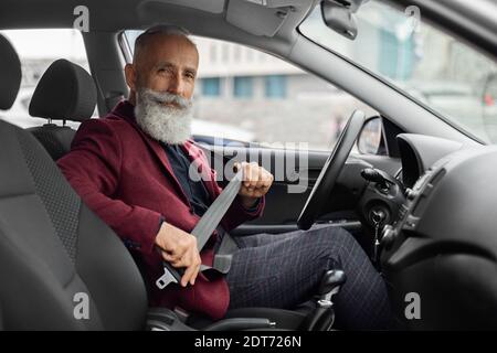 Senior man in suit fasten seat belt in his car Stock Photo