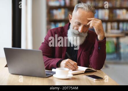 Pensive senior businessman checking his agenda, working at cafe Stock Photo