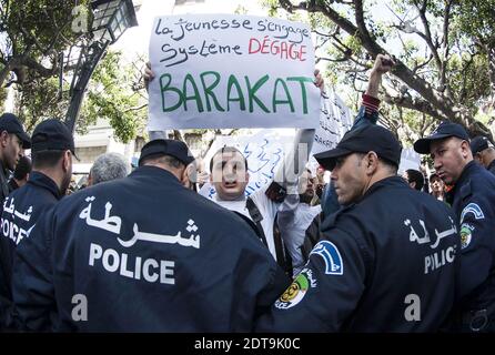 Algerian police stand guard as supporters of a movement called Barakat (meaning in Arabic 'That's enough'), campaigning for new leadership in Algeria, demonstrate holding banners and shouting slogans against Algeria's current President Bouteflika Abdelaziz running for a fourth term in the April 17 elections, outside the central school in downtown Algiers on March 27, 2014. The 77-year-old leader's decision to seek re-election despite serious health problems, which confined him to hospital in Paris for three months last year, has drawn heavy criticism not only in opposition ranks but also from Stock Photo