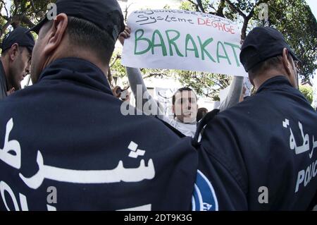Algerian police stand guard as supporters of a movement called Barakat (meaning in Arabic 'That's enough'), campaigning for new leadership in Algeria, demonstrate holding banners and shouting slogans against Algeria's current President Bouteflika Abdelaziz running for a fourth term in the April 17 elections, outside the central school in downtown Algiers on March 27, 2014. The 77-year-old leader's decision to seek re-election despite serious health problems, which confined him to hospital in Paris for three months last year, has drawn heavy criticism not only in opposition ranks but also from Stock Photo