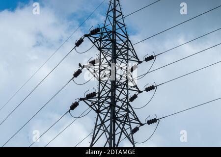 High voltage electric pylon and power lines against dark bloomy grey clouds. Stock Photo