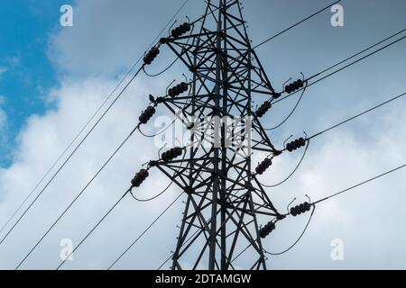 High voltage Electric tower pole silhouette and power lines against dark bloomy grey clouds. Stock Photo