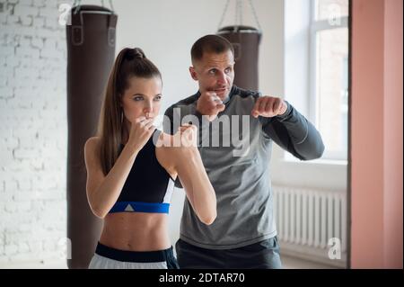 An experienced trainer puts the technique of blows to a young girl in the boxing hall Stock Photo