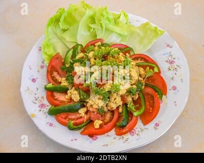 Meal of breakfast comprised of scrambled eggs, celery, and kale in the center of green sweet pepper and red ripe tomatoes arrainged in circle. Stock Photo