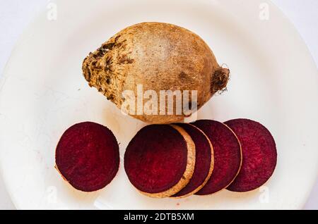 On white background beside a whole beetroot are slices laid out in a line with thier cross section upward. Stock Photo