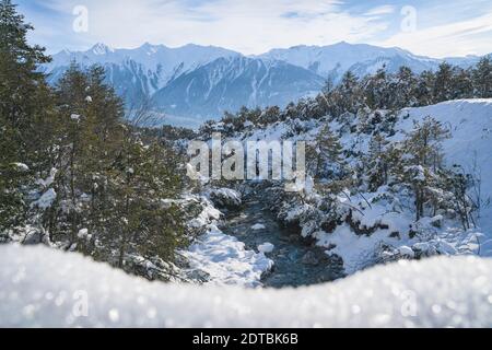 Sunny winter landscape in deep sparkling snow and evergreen trees with mountain river in Austrian Alps, Mieming, Tyrol, Austria Stock Photo