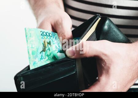 Man in a striped T-shirt holding a black leather wallet with kazakhstan banknotes. Stock Photo