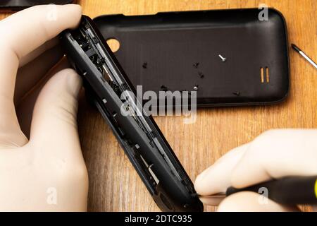 The master with a screwdriver disassembles a mobile phone on the table Stock Photo
