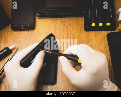 The master with a screwdriver disassembles a mobile phone on the table Stock Photo