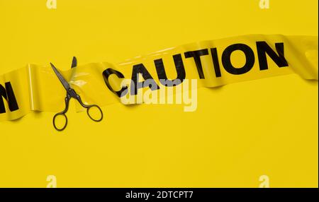 Studio shot of old fashioned scissors cutting caution tape on yellow background Stock Photo