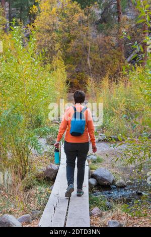 WOMAN HIKING OVER STREAM IN BANDELIER NATIONAL MONUMENT, NM, USA Stock Photo