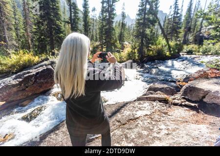 USA, Idaho, Stanley, Senior female hiker photographing stream Stock Photo
