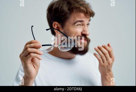 a man with narrowed eyes holds glasses in his hand on a light background vision problems Stock Photo