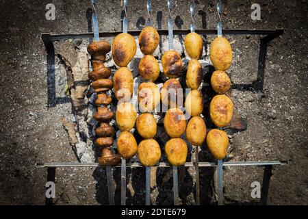 Potatoes and mushrooms are fried on the grill. Fresh and juicy potatoes with mushrooms cooked on fire. Milk potatoes and champignon mushrooms are frie Stock Photo