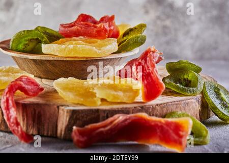 Dried fruits: Yellow candied pineapple rings, red papaya and green kiwi on a wooden board and in a wooden plate Stock Photo