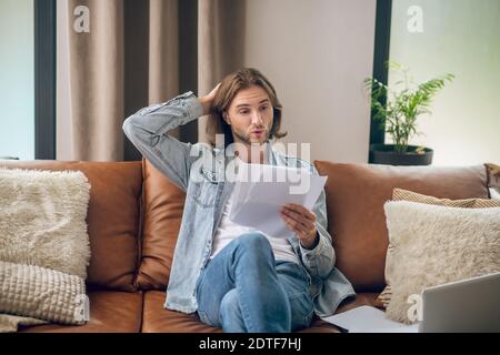 Young man in jeans shirt holding papers and looking thoughtful Stock Photo