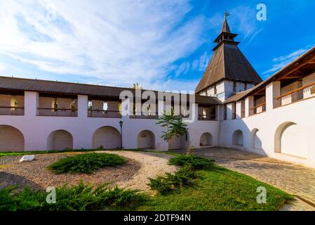 White stone wall of the courtyard with large arches and a wooden roof along the road with masonry in cloudy weather with blue clouds. Historical and a Stock Photo