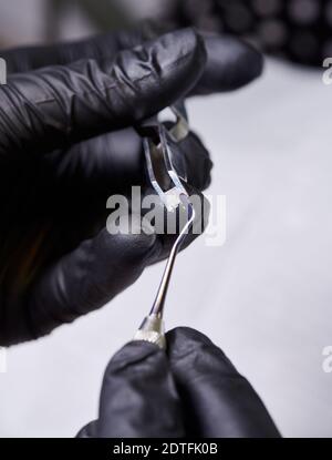 Macro shooting of orthodontic ceramic bracket in dentist's hands wearing black latex gloves. Process of putting adhesive paste on bracket before installation. Orthodontic accessories concept Stock Photo