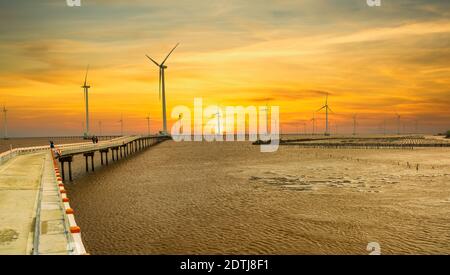 Clean energy, wind power plant in sunset sky with a pathway to the giant wind turbines at sea to provide electricity for human life. Stock Photo