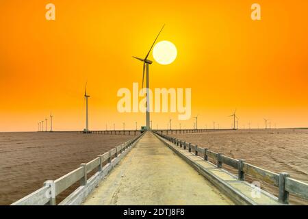 Clean energy, wind power plant in sunset sky with a pathway to the giant wind turbines at sea to provide electricity for human life. Stock Photo
